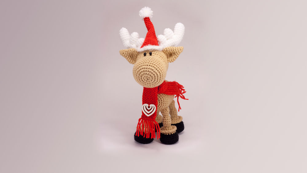 Обои для рабочего стола Вязанный позитивный олень в красной новогодней шапочке, шарфике с сердечком