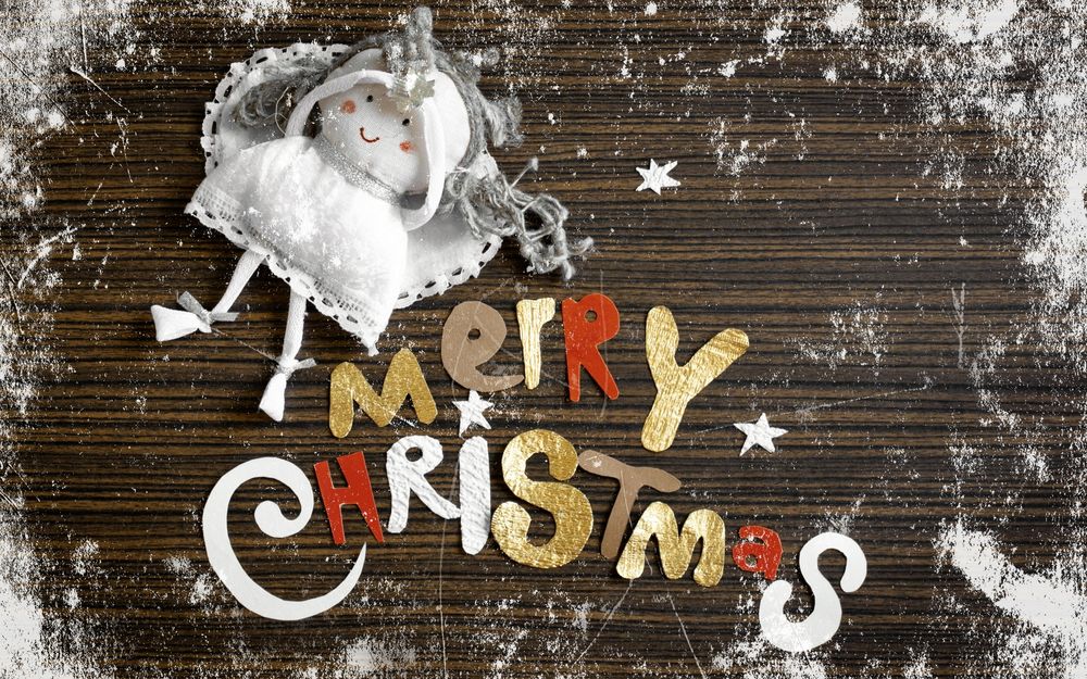Обои для рабочего стола Слова Merry Christmas / Веселого Рождества, вырезанные из разноцветной бумаги и кукольный ангел на деревянном столе, запорошенном снегом