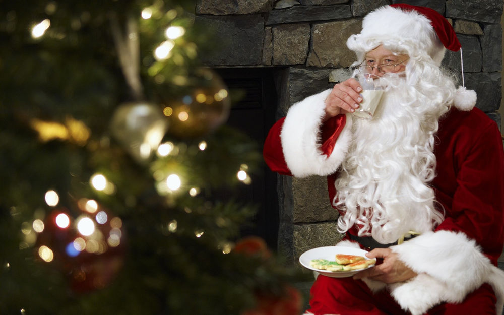 Обои для рабочего стола Санта Клаус / Santa Claus пьет молоко и ест печенье возле новогодней ёлки