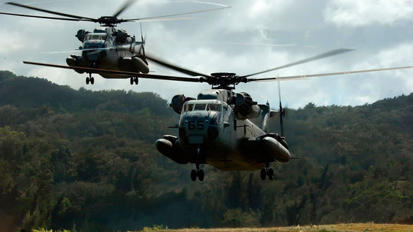 Обои на рабочий стол Пара боевых вертолетов американских ВВС CH-53D совершает полет над лесным массивом на фоне пасмурного небо со свинцовыми тучами