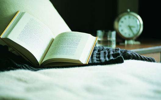 Обои на рабочий стол Открытая книга лежит на кровати, сзади неё на тумбочке видны часы и стакан с водой