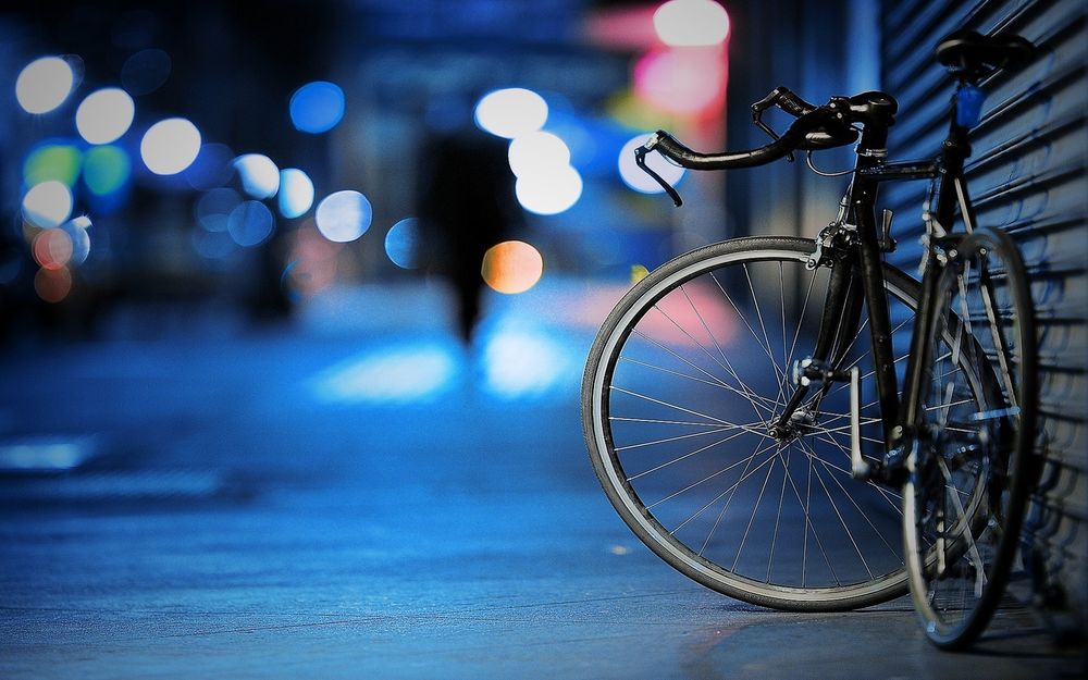 Обои для рабочего стола Велосипед припаркован на ночной улице города и силуэт уходящего человека