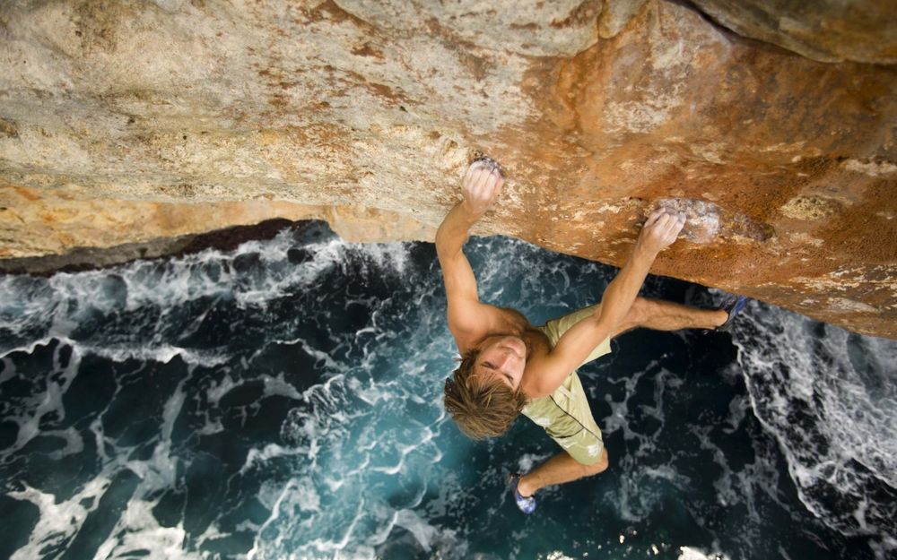 Обои для рабочего стола Chris Sharma / Крис Шарма держится за край скалы, вот-вот упадёт в море