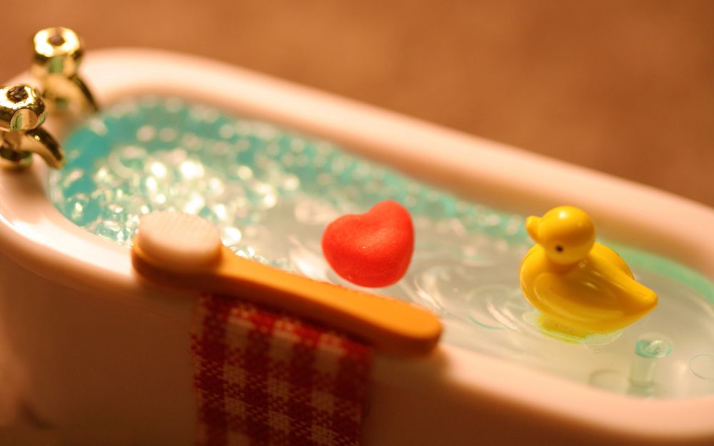 Обои для рабочего стола Игрушечная ванная, в которой плавают игрушечная утка и сердце, на краю лежат полотенце и щетка