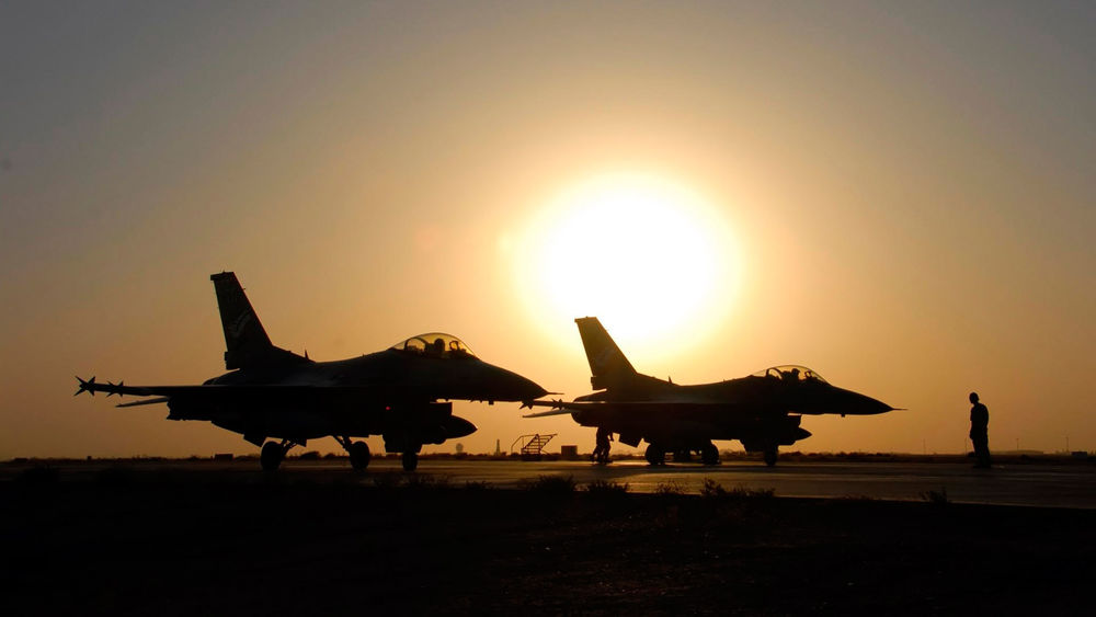 Обои для рабочего стола Силуэты двух истребителей и мужчины-авиатехника перед взлетом на фоне заката солнца