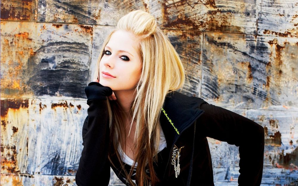 Обои для рабочего стола Певица Аврил Лавинь / Avril Lavigne улыбается, подперев подбородок рукой