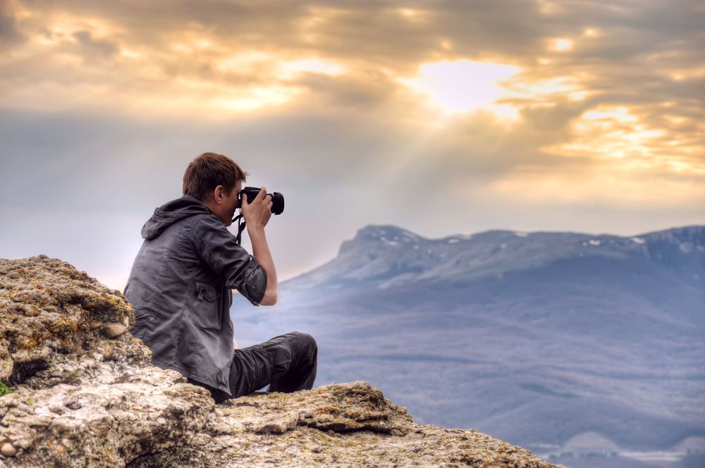 Обои для рабочего стола Мужчина сидит на камнях и фотографирует горы