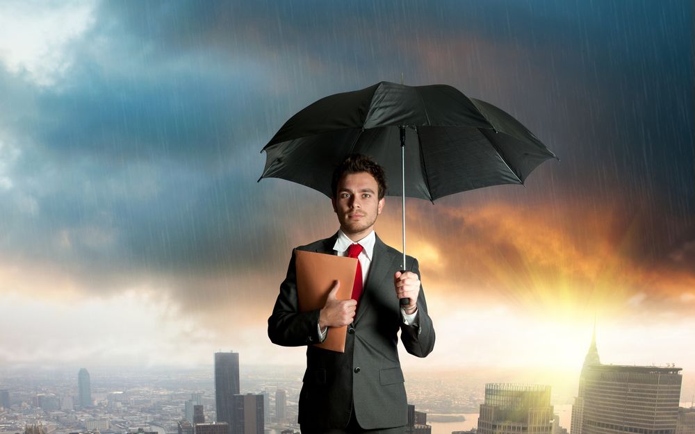 Обои для рабочего стола Мужчина в деловом костюме, с папкой в руках и под чёрным зонтом стоит на фоне города и тёмных туч с которых идёт дождь