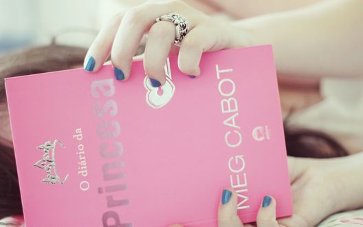 Обои на рабочий стол Девушка читает книгу Мэг Кэбот / Meg Cabot  'Дневники принцессы' / 'O diaro da Princesa' на испанском языке в розовой обложке