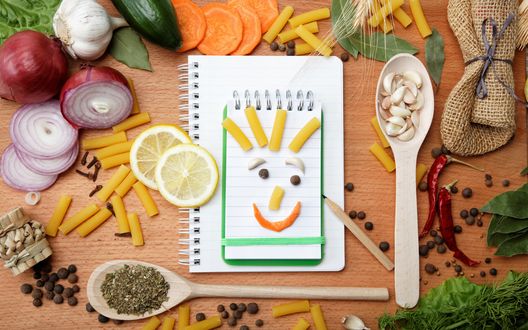 Обои на рабочий стол Веселая кухня, на блокноте разложены кусочки еды в виде улыбающейся рожицы, вокруг овощи и фрукты