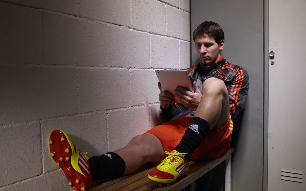 Обои для рабочего стола Известный футболист Лионель Месси /  Lionel Messi сидит с планшетом в руках на лавке в раздевалке