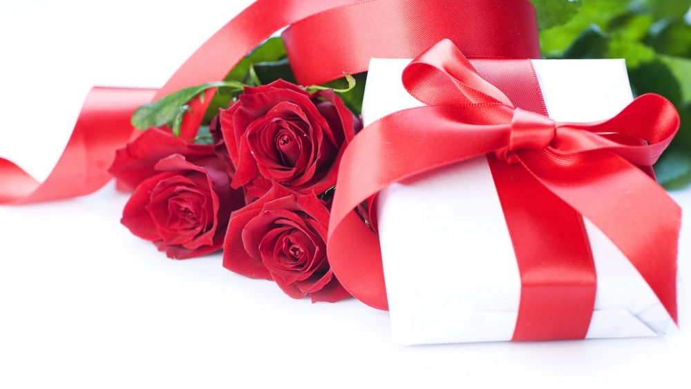 Обои для рабочего стола Букет красных роз лежит рядом с подарком на белом фоне