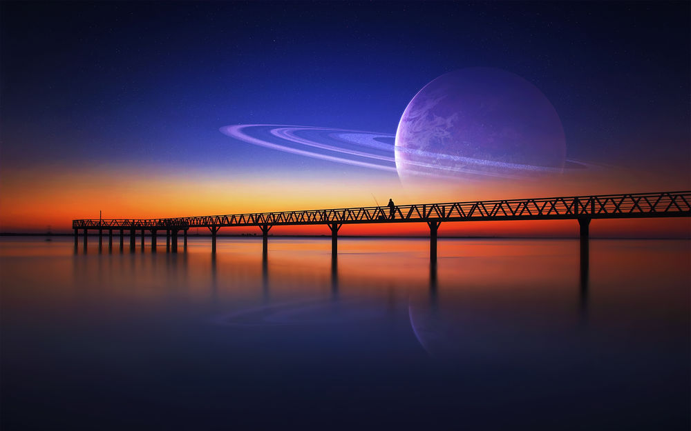Обои для рабочего стола Рыбак с удочкой стоит на мосту океанского побережья на фоне заката с изображением планеты Сатурн