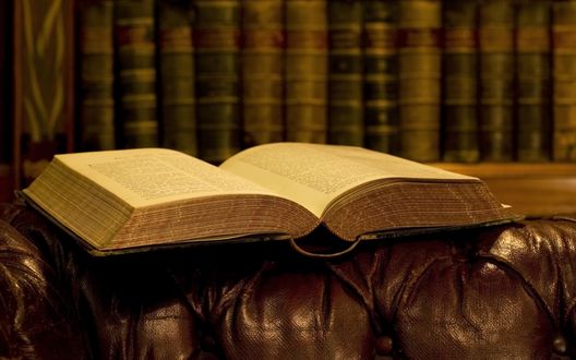 Обои на рабочий стол Открытая книга лежит на кожаном диване на фоне других книг