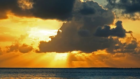 Обои на рабочий стол Солнце светит из - за облаков на море