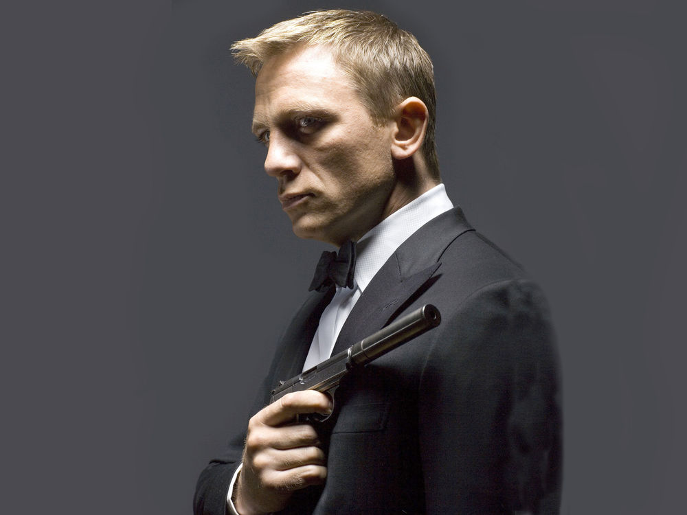 Обои для рабочего стола Дэниэл Крэйг / Daniel Craig в роли агента 007, Джеймса Бонда / James Bond в смокинге с пистолетом на сером фоне