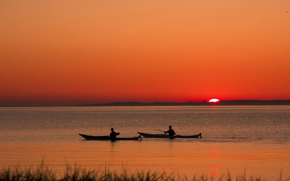 Обои для рабочего стола Двое спортсменов проводят тренировку на байдарках на озере на фоне заходящего солнца