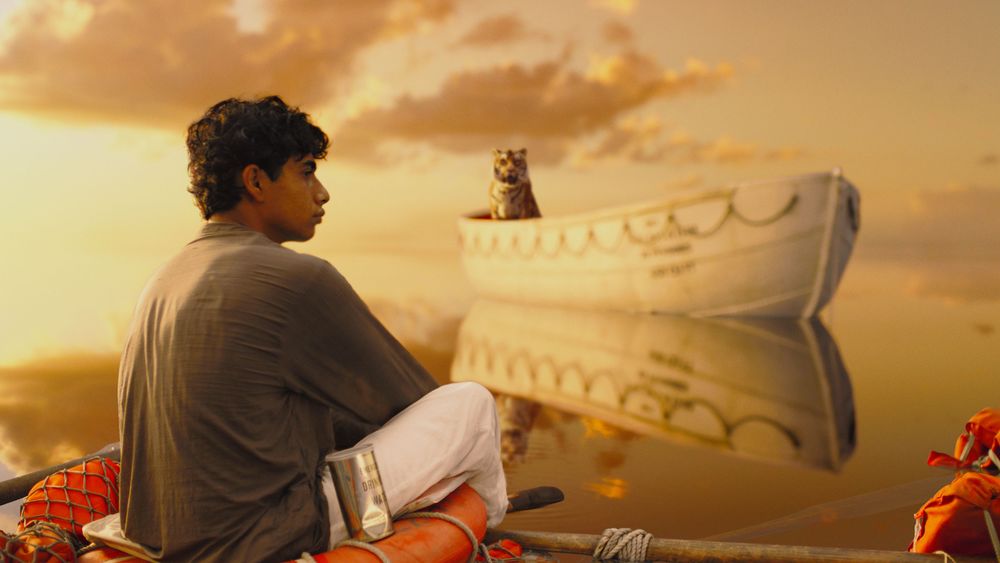 Обои для рабочего стола Аюш Тандон /  Ayush Tandon сидит на плоту на него из лодки смотрит тигр из кинофильма ''Жизнь Пи'' / ''Life of Pi''