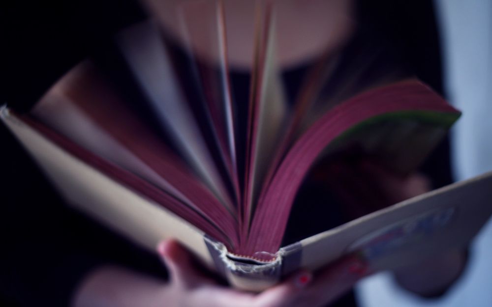 Обои для рабочего стола Девушка листает книгу с красными страницами