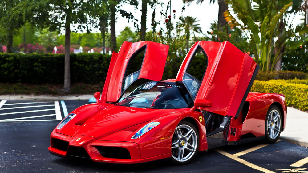 Обои для рабочего стола Автомобиль Ferrari Enzo красного цвета стоит на парковке у пальмовой рощи