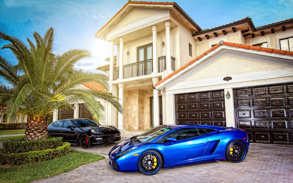 Обои для рабочего стола Автомобили Lamborghini Mansion и Porsche Cayenne стоят у большого двухэтажного дома с колоннами и двумя гаражами