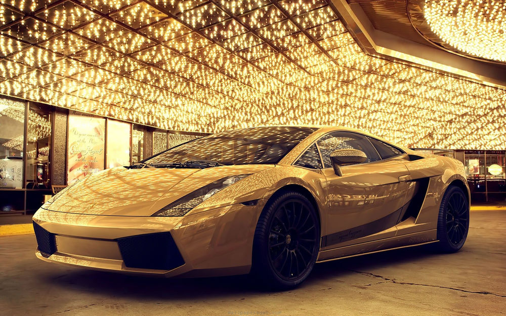 Обои для рабочего стола Автомобиль Lamborghini Aventador желтого цвета стоит под сверкающим огнями зданием
