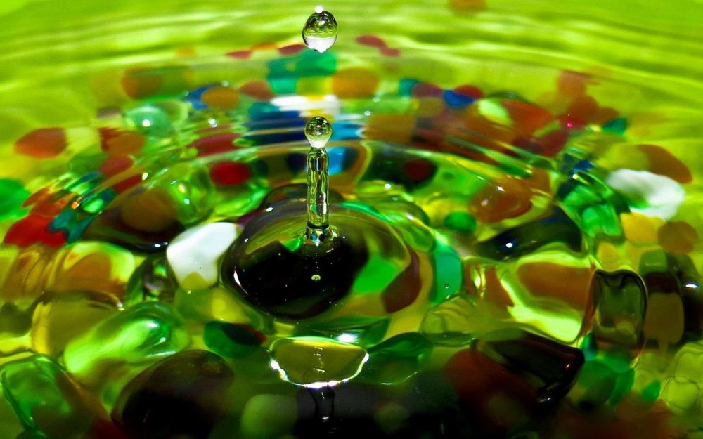 Обои для рабочего стола Капля падает в воду, на дне которой лежат разноцветные камушки