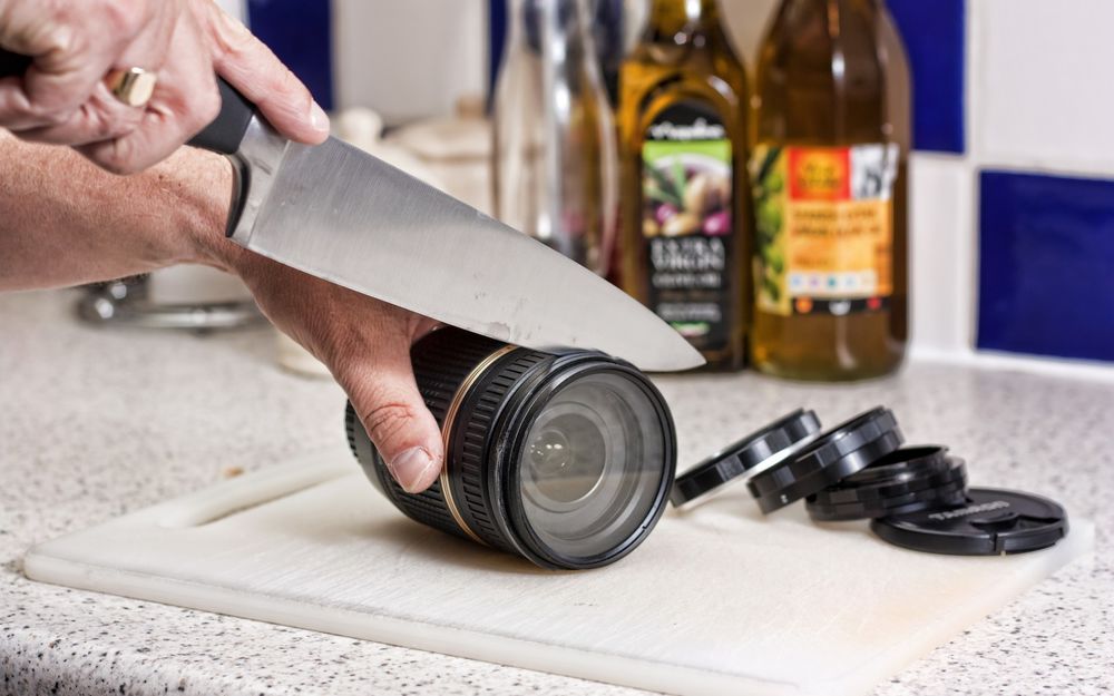 Обои для рабочего стола Мужчина нарезает линзу фотокамеры большим ножом на кухонном столе