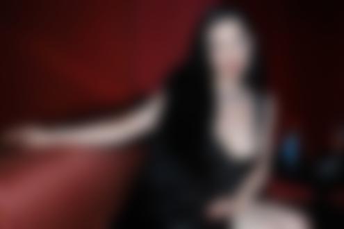 Обои на рабочий стол Dita Von Teese / Дита фон Тиз в черном платье с ожерельем на шее, сидит на диване мило улыбаясь