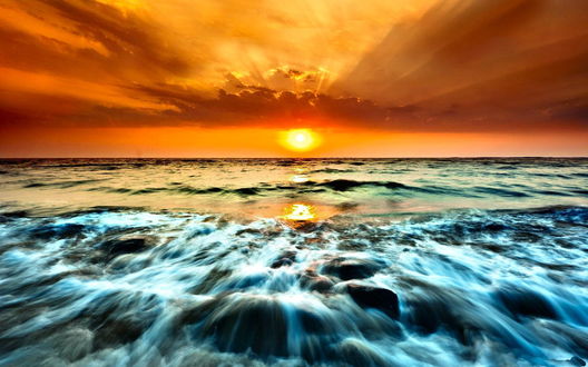Обои на рабочий стол Заходящее над морем солнце с пенистой водой у береговых камней