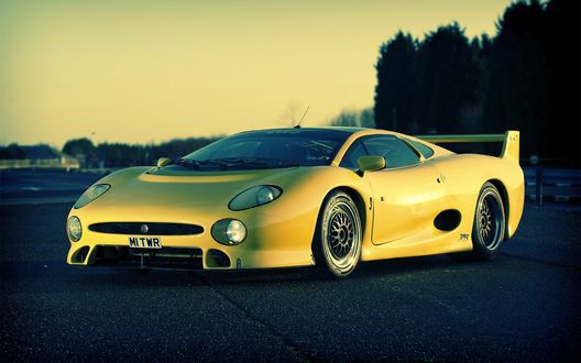 Обои на рабочий стол Желтый автомобиль Jaguar XJ220 / Ягуар XJ220 на фоне неба и деревьев