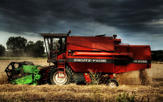 Обои на рабочий стол Немецкий зерноуборочный комбайн Deutz - Fahr / Дойц Фар, работающий на пшеничном поле на фоне темного грозового неба