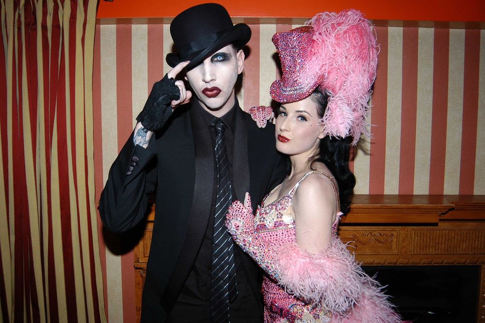 Обои для рабочего стола Dita Von Teese / Дита фон Тиз в розовом наряде стоит рядом с Marilyn Manson / Мэрли Менсоном, который одет в черный костюм