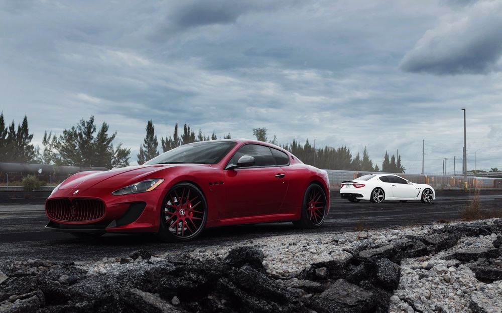 Обои для рабочего стола Красная и белая машины Maserati GranTurismo / Мазерати ГранТуризмо стоят на дороге, на фоне деревьев и облаков