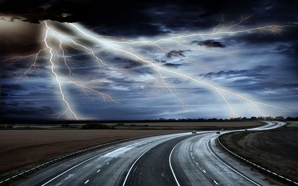 Обои для рабочего стола Машины едут по мокрой дороге на фоне молний в небе