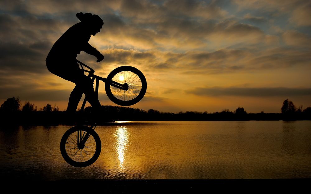Обои для рабочего стола Мужчина на велосипеде ездит на фоне озера и неба