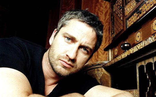 Обои на рабочий стол Актер Gerard Butler / Джерард Батлер смотрит в камеру, сидя у бюро