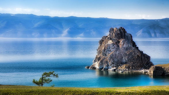 Обои на рабочий стол Красивое скальное образование, стоящее возле берега морской бухты, окруженного горами и одиноко стоящего на берегу дерева