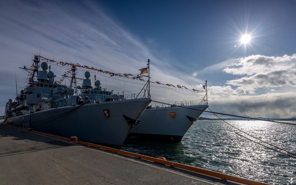 Обои для рабочего стола Военные корабли, стоящие у пирса на фоне неба и яркого света солнца
