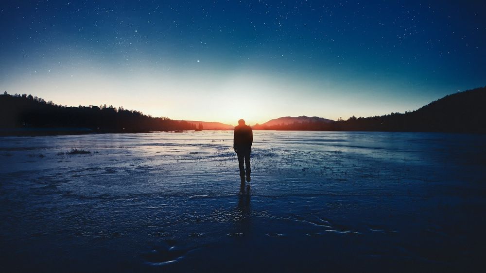 Обои для рабочего стола Одинокий парень идет по замерзшей реке на фоне звездного неба
