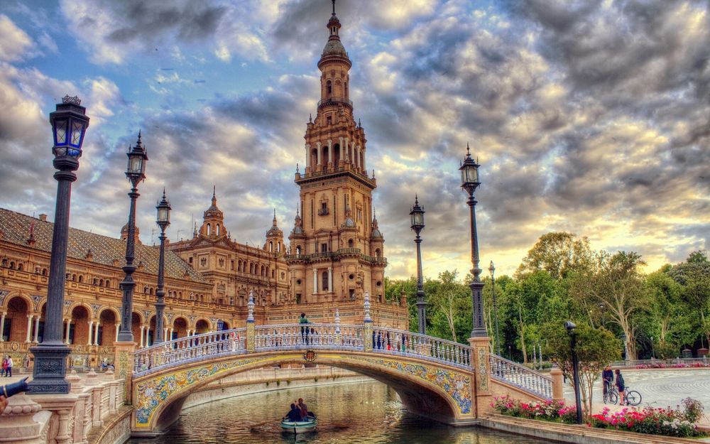 Обои для рабочего стола Площадь Испании / Plaza de Espana в Севилье / Seville с архитектурным выставочным комплексом, окруженный водоемом, через который пролегает мост и по бокам стоят фонари, фотограф Иисус Санчес / Jesus Sanches, Испания / Spain