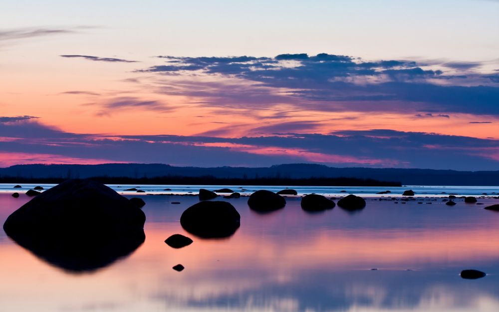 Обои для рабочего стола Камни торчат из озера, в котором отражается вечернее небо на закате