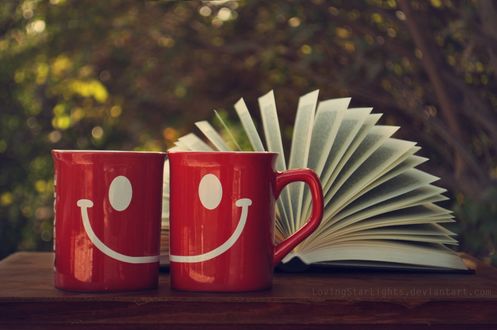 Обои на рабочий стол Две чашки с рисунком улыбки стоят перед открытой книгой, автор MintLights