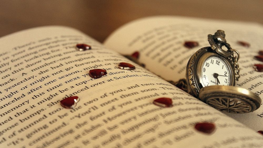 Обои для рабочего стола Карманные часы лежат на страницах открытой книги в окружение пластмассовых сердечек
