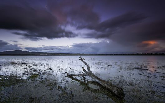Обои на рабочий стол Темное ночное небо с облаками, через которые видно луну, над рекой