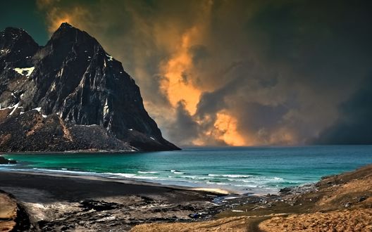 Обои на рабочий стол Красивая морская бухта со скалистыми берегами, вершинами гор, местами покрытых снегом, лазурным отливом морской воды на фоне предгрозового неба с темными, свинцовыми тучами