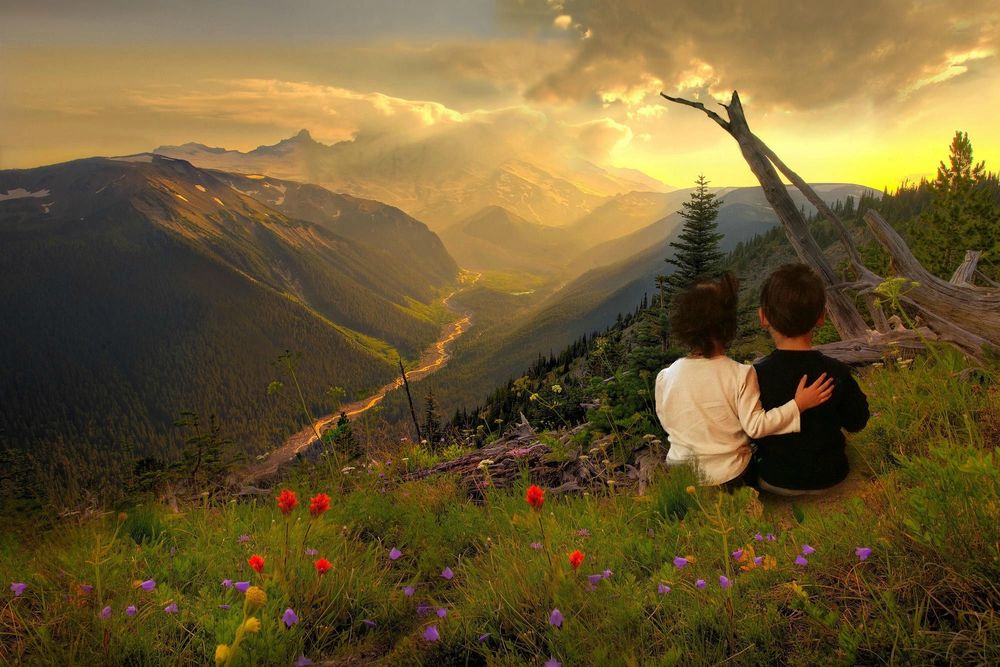 Обои для рабочего стола Мальчик и девочка сидят и смотрят на горы в облаках и лучах заходящего солнца