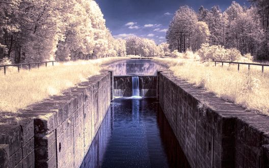 Обои на рабочий стол Водный канал с искусственно созданным водопадом, отвесными каменными стенами, деревьями, окружающими это гидротехническое сооружение, с густой кроной, покрытой густым слоем белого инея на фоне синего неба с небольшими белыми облаками