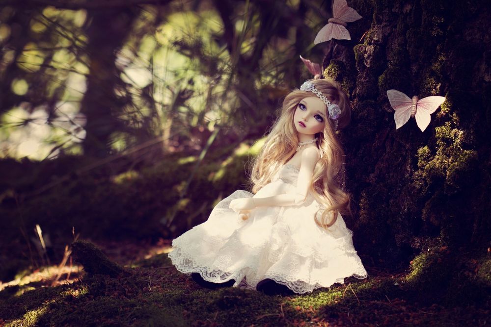Обои для рабочего стола Кукла в белом свадебном платье, сидящая возле ствола дерева в окружении бабочек