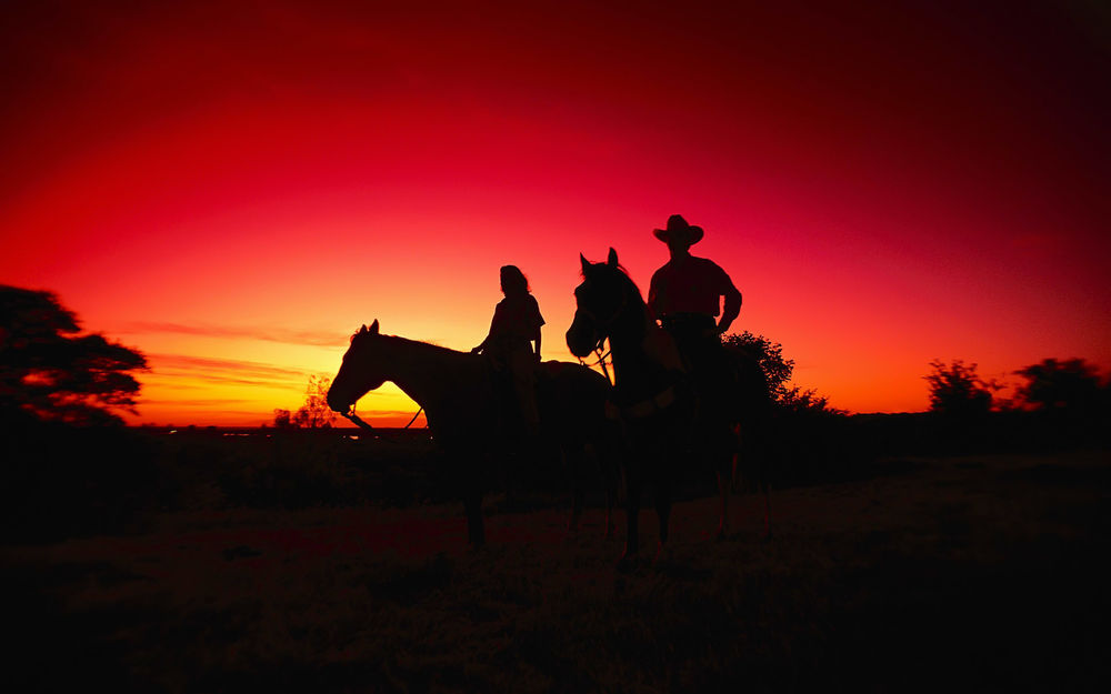 Обои для рабочего стола Девушка и мужчина в ковбойской шляпе на лошадях на фоне закатного неба